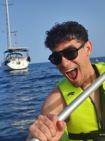 A close-up of a smiling tourist wearing a helmet and life jacket, holding a paddle on a sunny day.