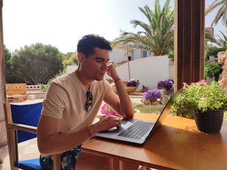A person working on a laptop at a cozy outdoor café with tropical plants around.