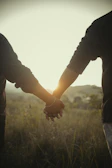A joyful couple holding hands, backlit by warm golden sunlight in an open field.