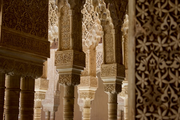 Intricate Moorish architecture with detailed carvings and arches, showcasing elaborate patterns and motifs. The stone pillars and walls are adorned with exquisite geometric and floral designs, creating a sense of historical richness and artistic mastery.
