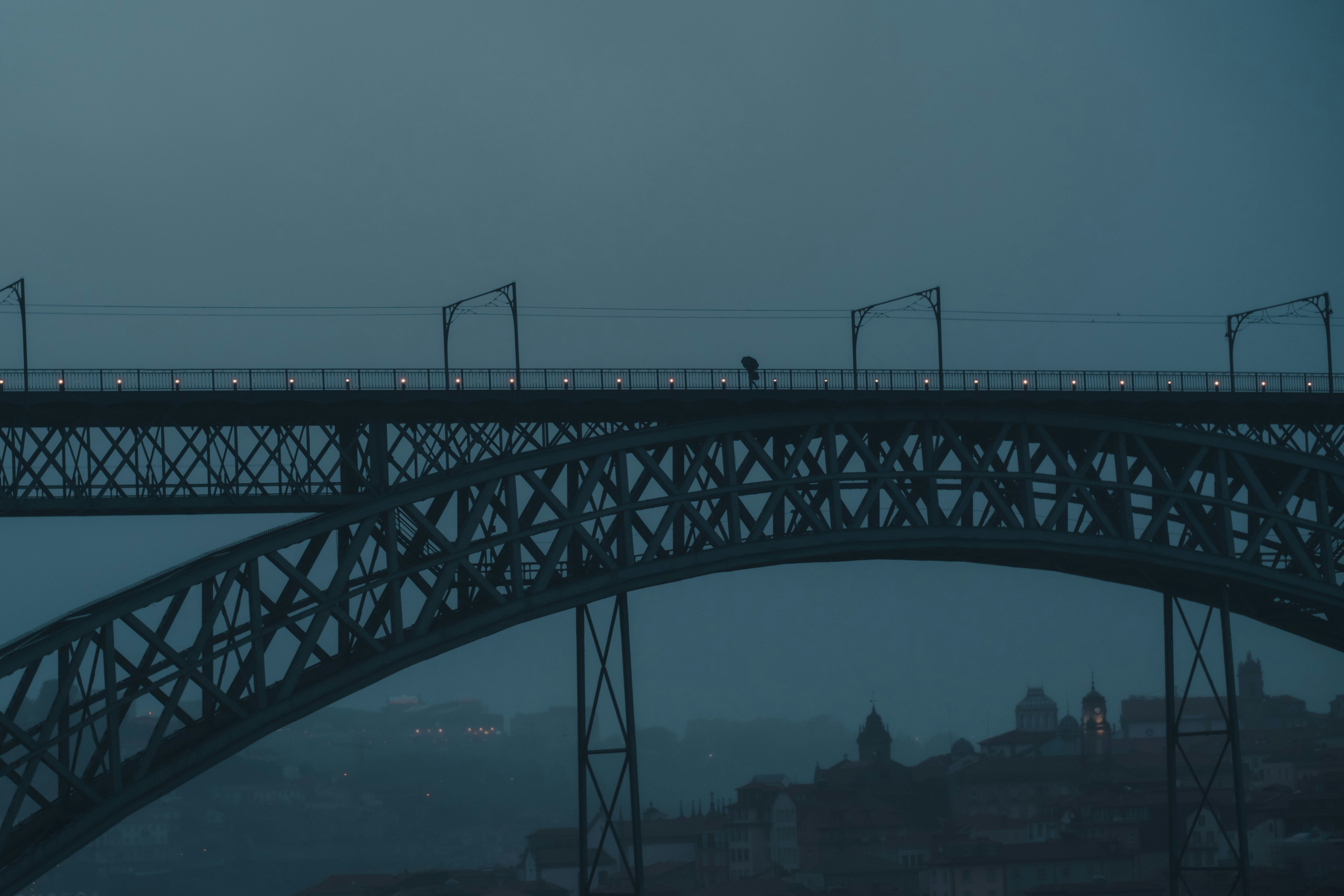 Man with umbrella crossing bridge on rainy morning.