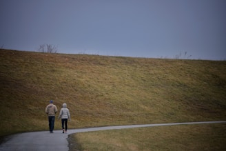 a man and woman walking on a road next to a hill