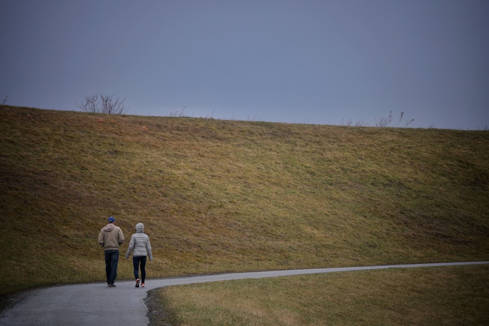 a man and woman walking on a road next to a hill