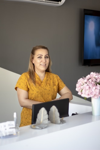 a woman standing a clinic reception desk wearing scrubs