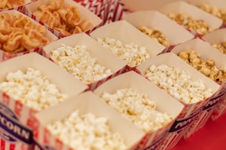 A neat arrangement of popcorn boxes filled with different varieties of popcorn, including classic buttered and a caramel-coated type. The boxes are designed with red and white striped patterns and are placed on a flat surface.