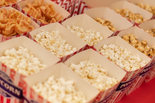 A neat arrangement of popcorn boxes filled with different varieties of popcorn, including classic buttered and a caramel-coated type. The boxes are designed with red and white striped patterns and are placed on a flat surface.