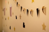 A wall features a decorative string garland with alternating black and gold triangular shapes. Surrounding the garland are cutouts of stars, movie cameras, and popcorn containers. The background is a warm beige color.