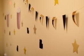 A wall features a decorative string garland with alternating black and gold triangular shapes. Surrounding the garland are cutouts of stars, movie cameras, and popcorn containers. The background is a warm beige color.