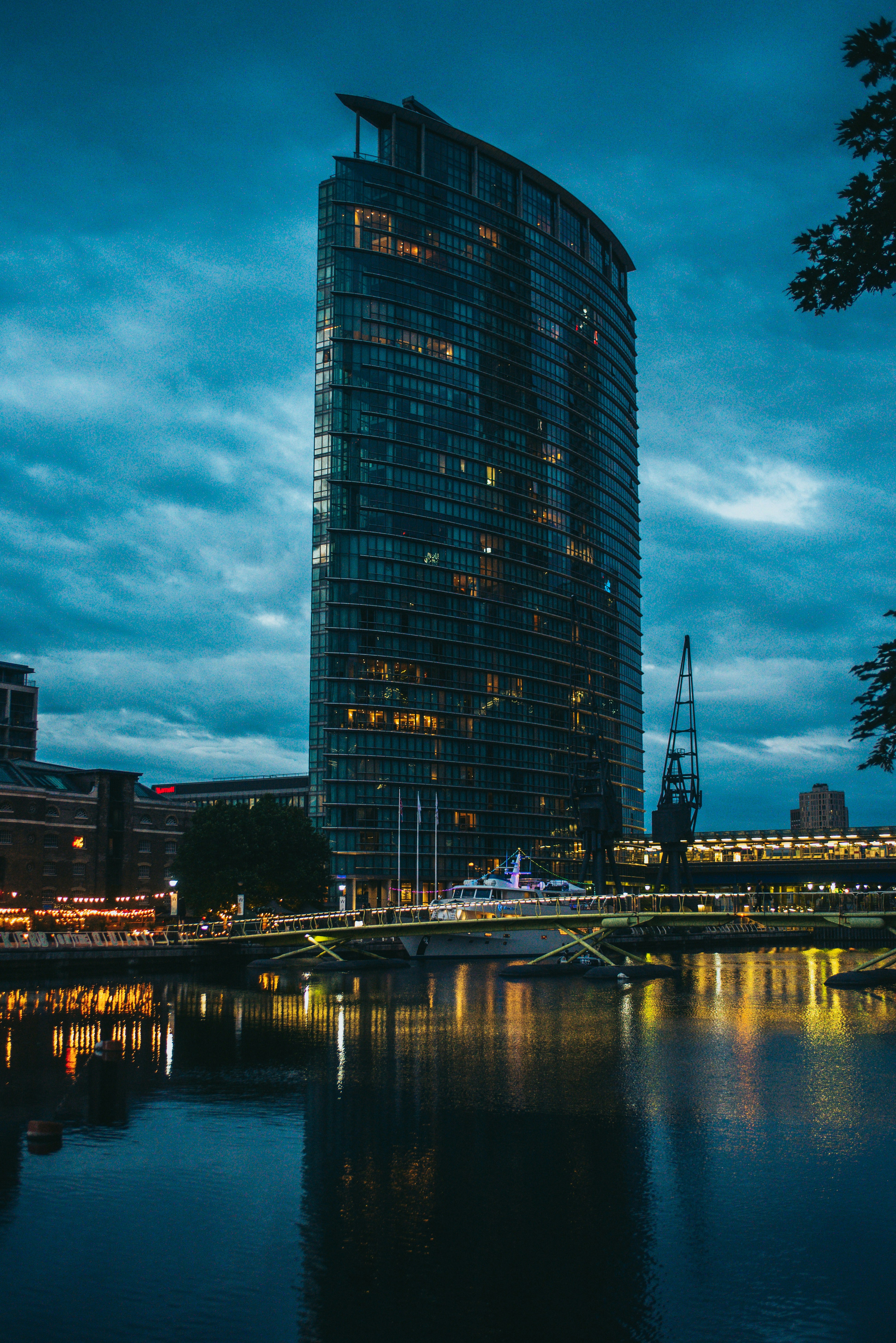 Modern glass tower skyscraper by the sea at night, dark moody sky, city lights reflecting on water