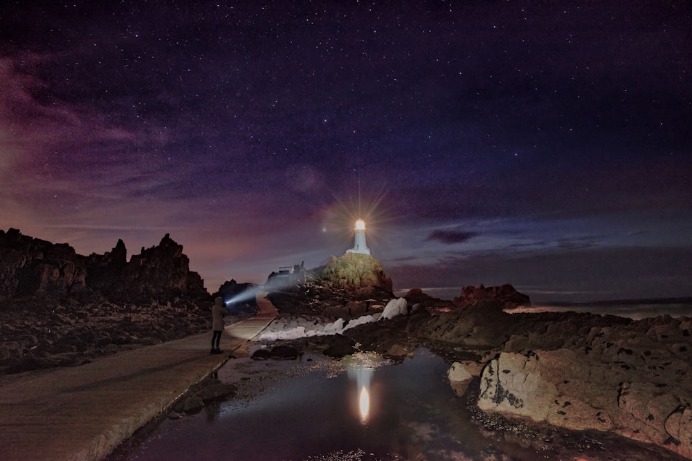 a person standing on a rocky beach with a bright light in the sky