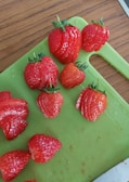 Fresh strawberries being diced on a cutting board next to a bowl of cheesecake filling.