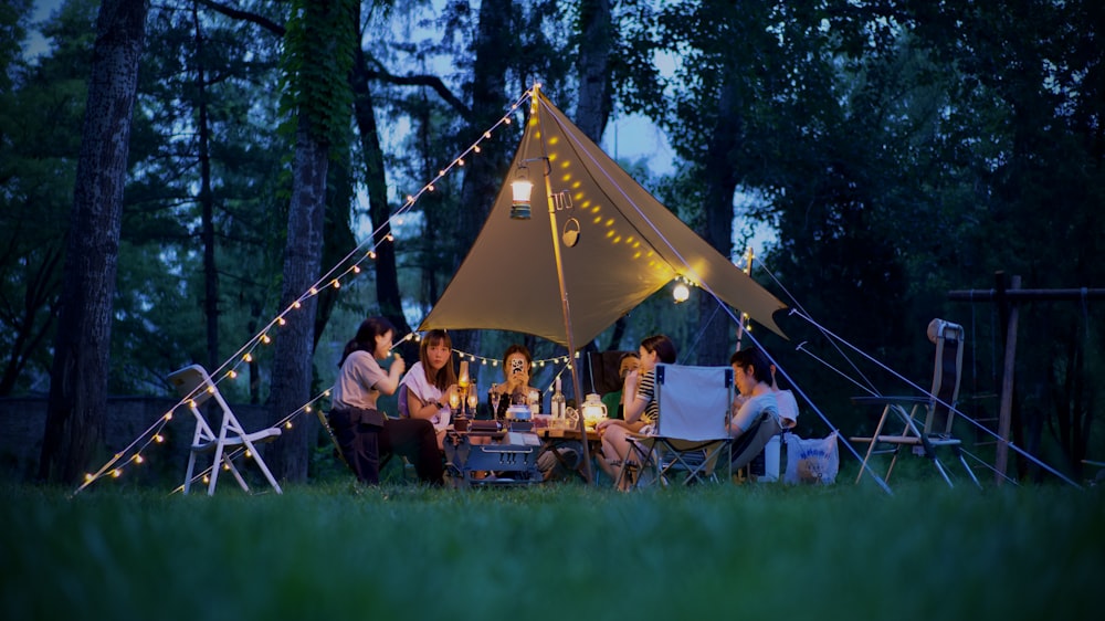 a group of people sitting around a tent in the woods