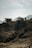Two modern, rectangular cabins are perched on a rugged, rocky hillside with sparse vegetation. The background features misty mountain silhouettes under a clear, blue sky.