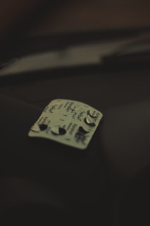 A blister pack of pills with a few tablets removed is resting on a dark surface. The pack has some text written on it, and the lighting is dim, creating a shadowy atmosphere.