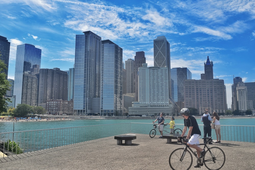 a group of people riding bikes on a bridge over water with a city in the background