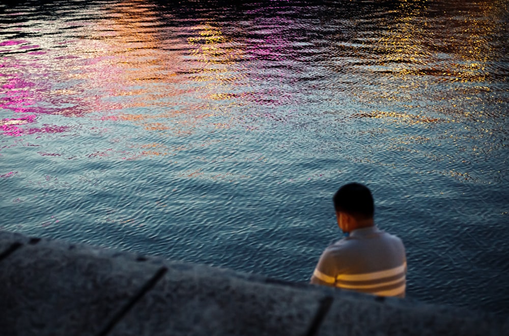 a man sitting on a ledge looking at the water