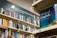 A bookshelf filled with a variety of books, primarily in English. The visible sign above the shelf indicates these are books in English, and several shelves are labeled with alphabetical markers. A large dictionary is prominently displayed, suggesting a focus on English language resources.