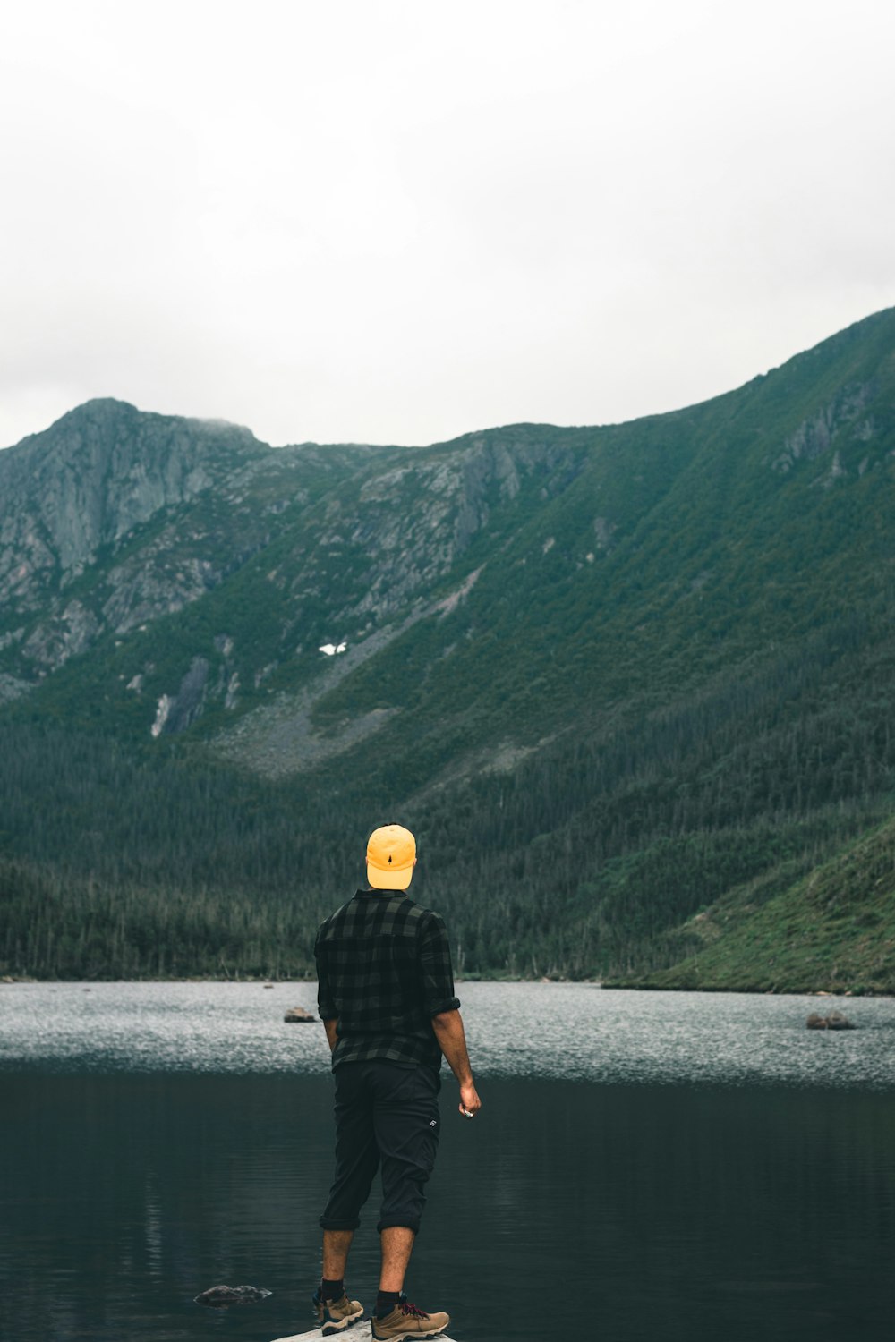 a man standing on a rock by a lake with mountains in the background