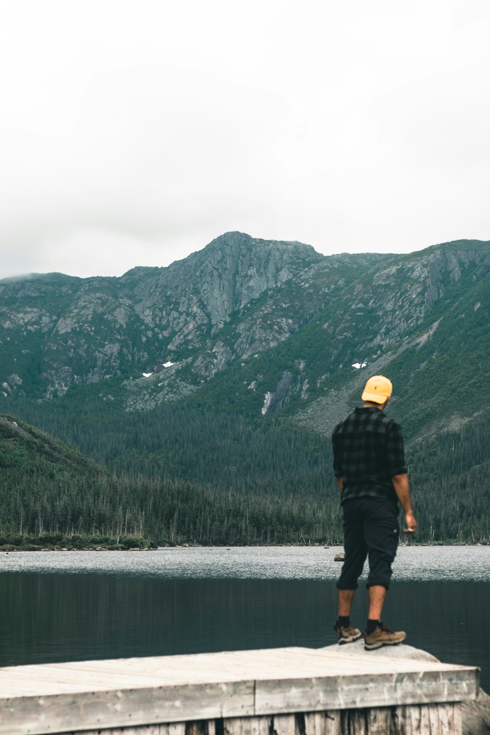 a man standing on a ledge overlooking a lake and mountains