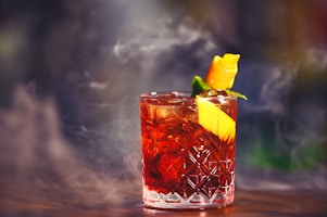 Moody shot of a burnished gold-rimmed glass filled with a deep crimson cocktail, garnished with a twist.