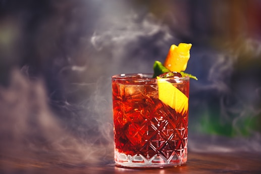 Moody shot of a burnished gold-rimmed glass filled with a deep crimson cocktail, garnished with a twist.