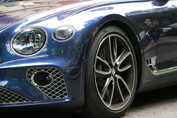 A close-up of a luxury car’s polished wheel and sleek body reflecting city lights.