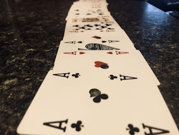 A line of playing cards arranged in a perspective view across a dark marbled surface, prominently featuring aces of clubs and hearts.