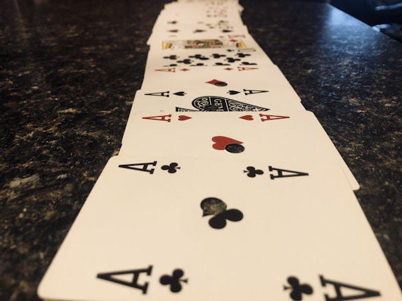 A line of playing cards arranged in a perspective view across a dark marbled surface, prominently featuring aces of clubs and hearts.