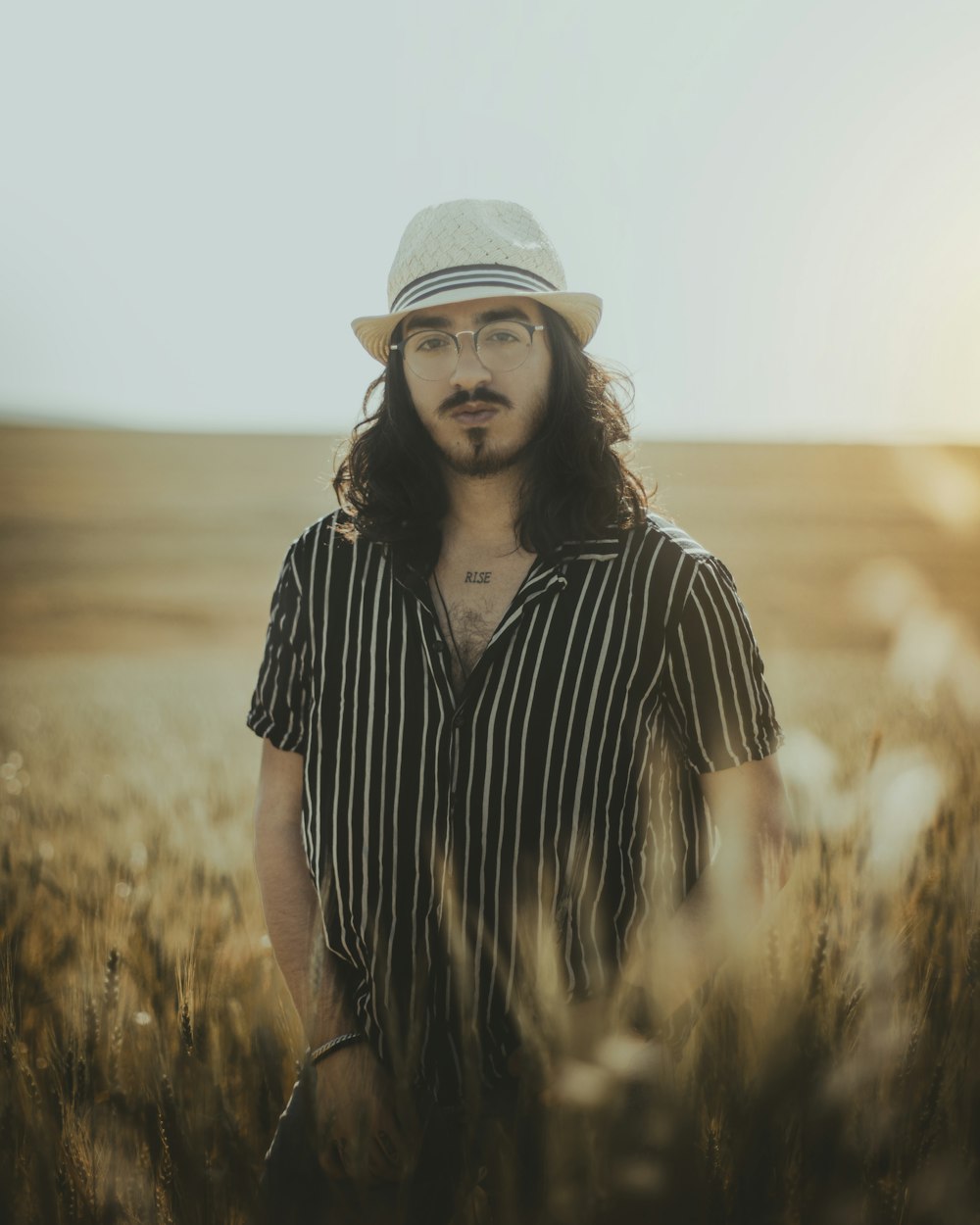 a person with long hair and a hat standing in a field