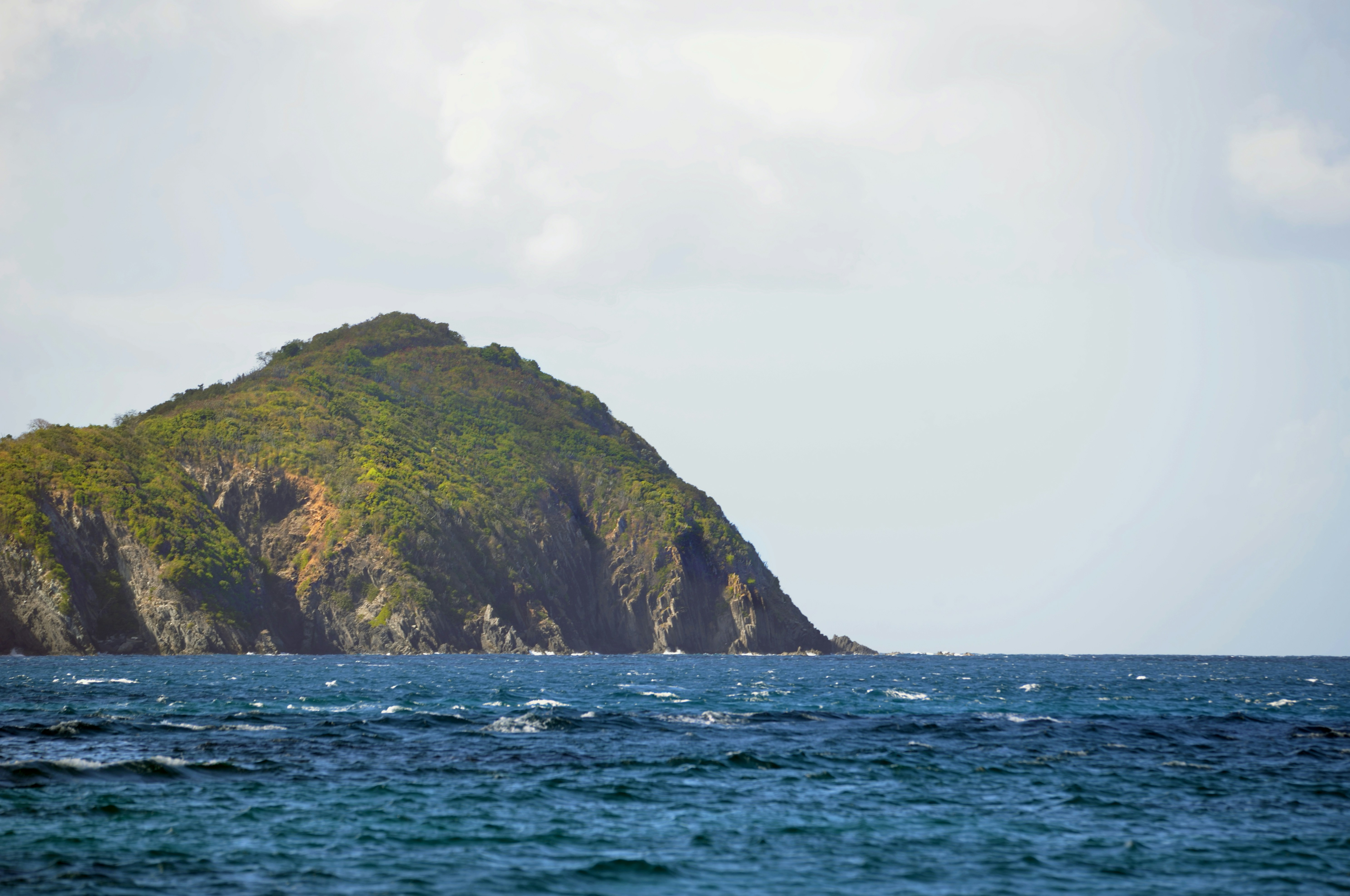 a large green cliff next to a body of water, An offshore Caribbean island cay surrounded by deep blue water.
