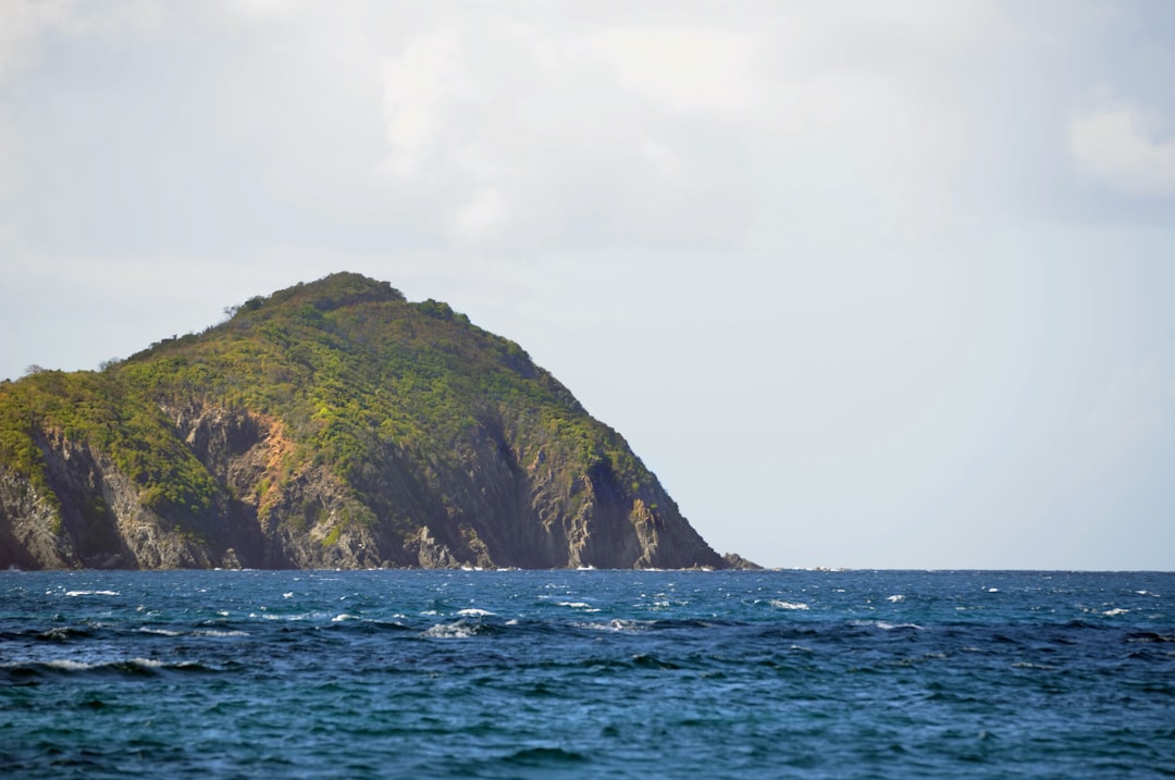 a large green cliff next to a body of water, An offshore Caribbean island cay surrounded by deep blue water.