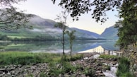 A peaceful lakeside scene with morning mist rolling over the water and distant mountains.