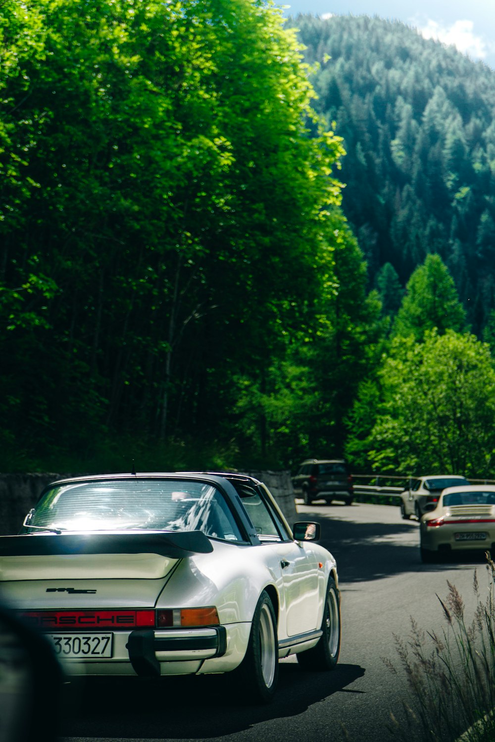 a white car on a road with trees and mountains in the background