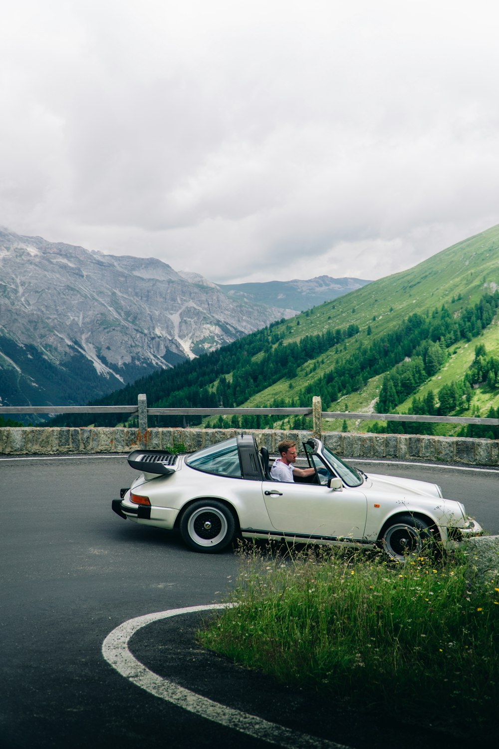 a person driving a convertible car on a road with mountains in the background