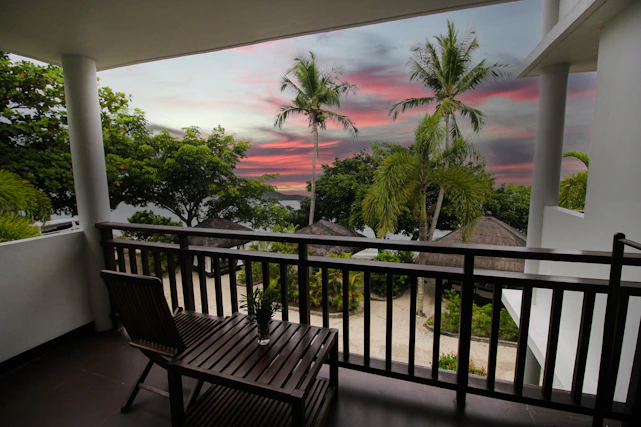 Cozy hotel room with a private balcony overlooking a serene garden at sunset