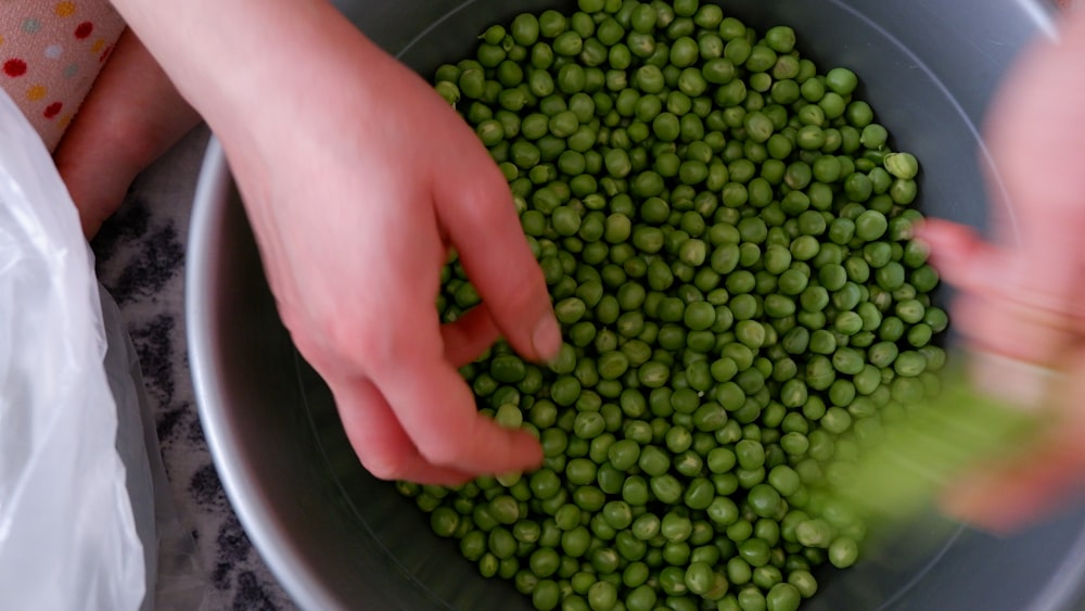 a person holding a bowl of peas