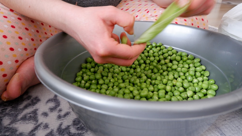 a person holding a bowl of peas