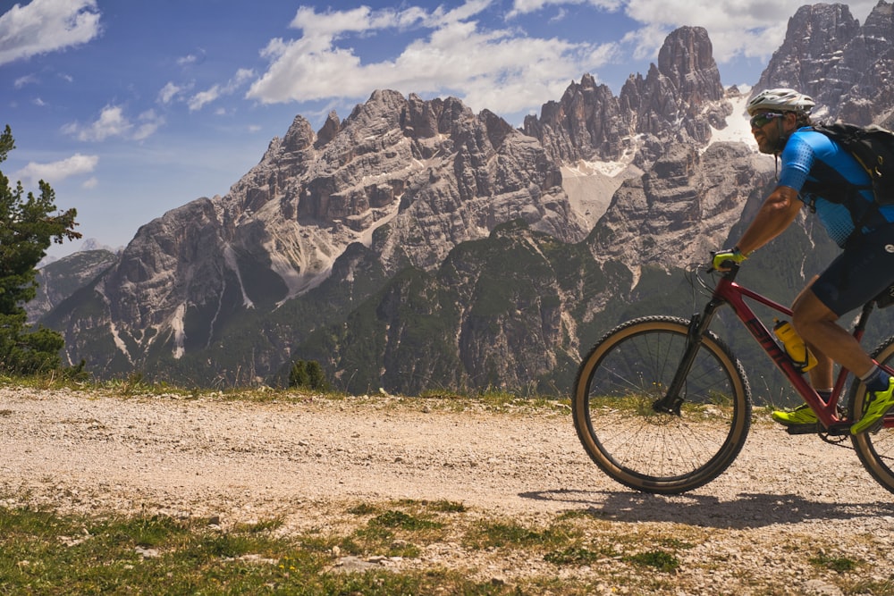 Un uomo in sella a una bicicletta su una strada sterrata di fronte a una montagna rocciosa