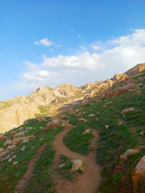 A serene mountain landscape with a winding trail under a bright blue sky.
