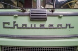 The front of a vintage vehicle features a prominent metal emblem with the name 'Chausson' displayed on its light green surface. The design includes metallic elements and a classic style grille.