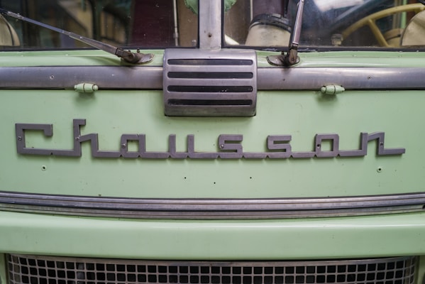 The front of a vintage vehicle features a prominent metal emblem with the name 'Chausson' displayed on its light green surface. The design includes metallic elements and a classic style grille.
