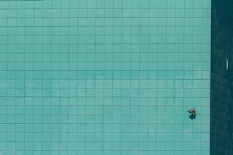 A grid of teal tiles covers the surface, with a single security camera mounted on the lower right. The tiles create a geometric pattern that is uniform across the wall.