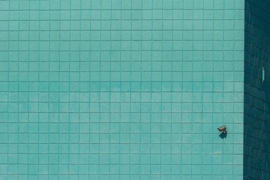 A grid of teal tiles covers the surface, with a single security camera mounted on the lower right. The tiles create a geometric pattern that is uniform across the wall.