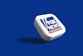 A three-dimensional representation of the Fox News Channel logo positioned diagonally on a blue background. The logo consists of the words 'FOX NEWS' in white text on a dark blue square, with red and white elements at the bottom.