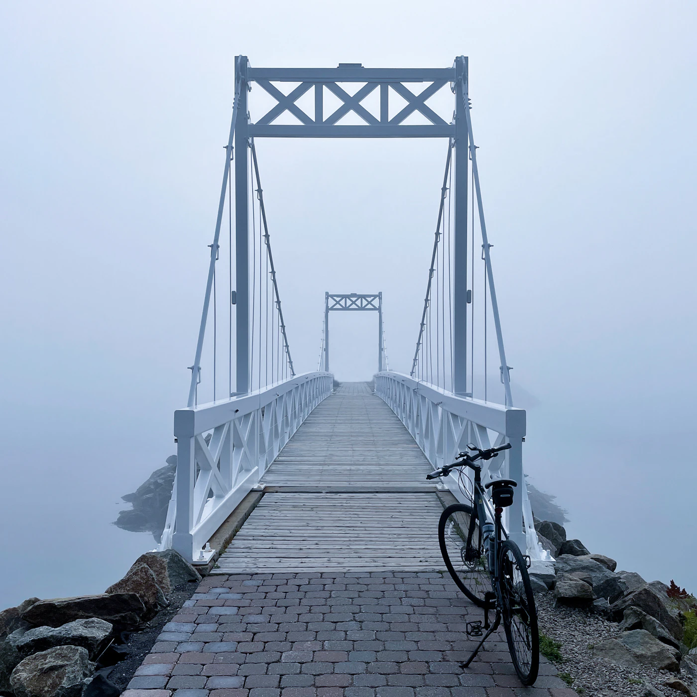 A bicycle leaning against the railing of a bridge in morning mist