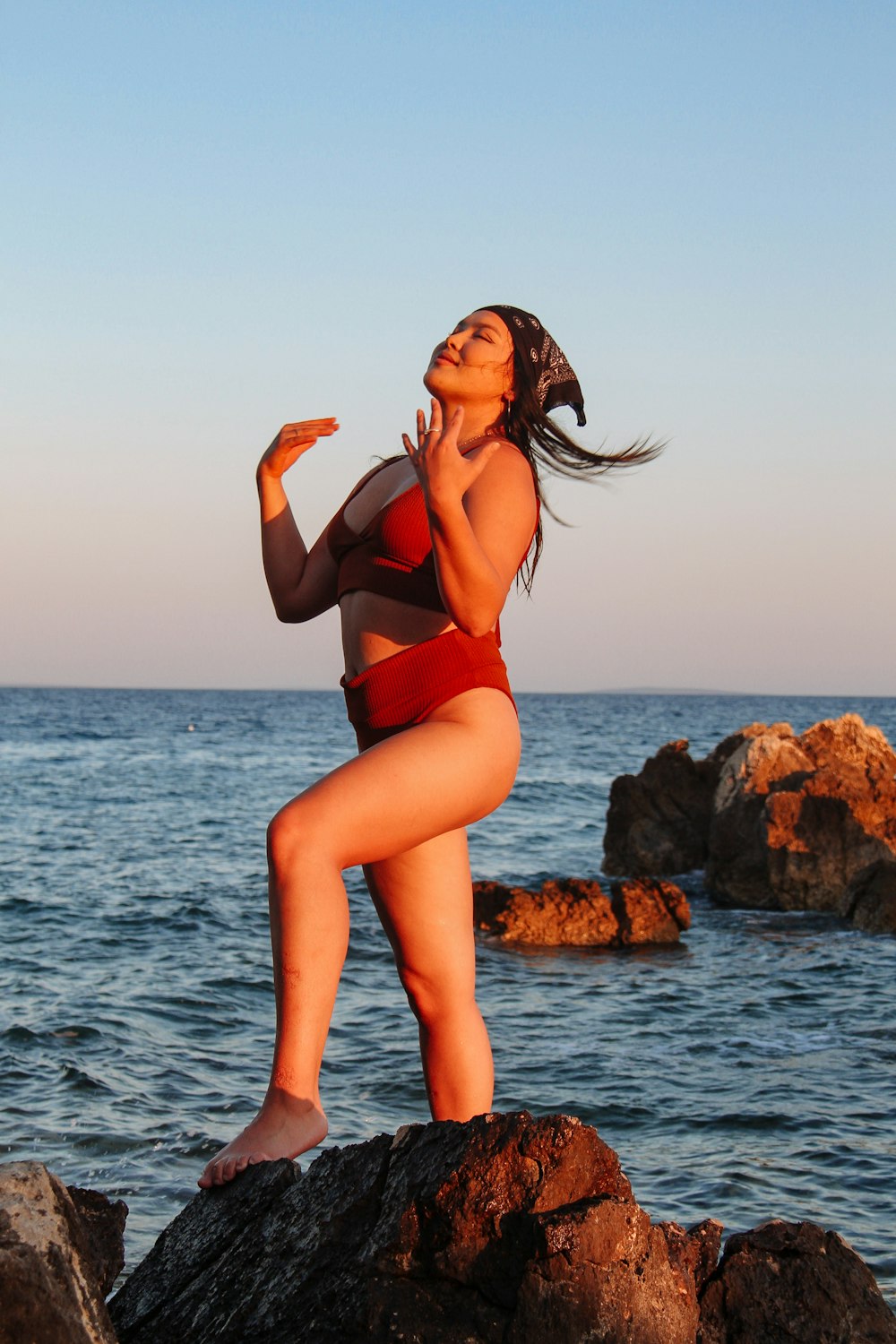 a woman in a garment standing on rocks by the water