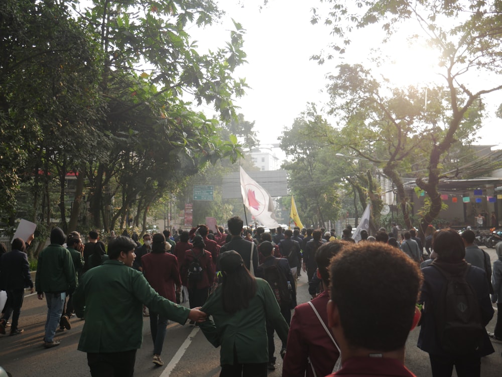 a group of people walking on a street with trees and buildings