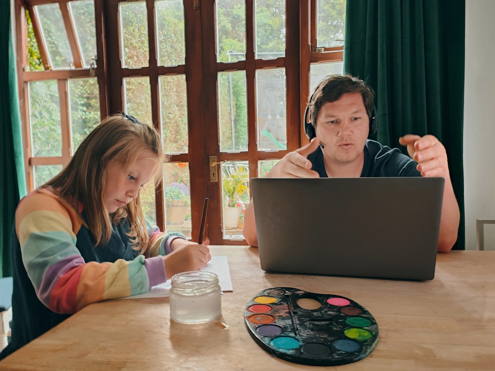 a woman and a girl sitting at a table with a laptop