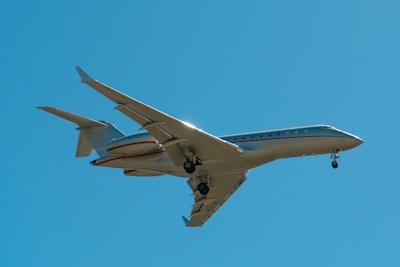 A private jet with extended landing gear flies against a clear blue sky, capturing the sleek design and modern engineering of the aircraft.