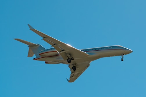 A private jet with extended landing gear flies against a clear blue sky, capturing the sleek design and modern engineering of the aircraft.